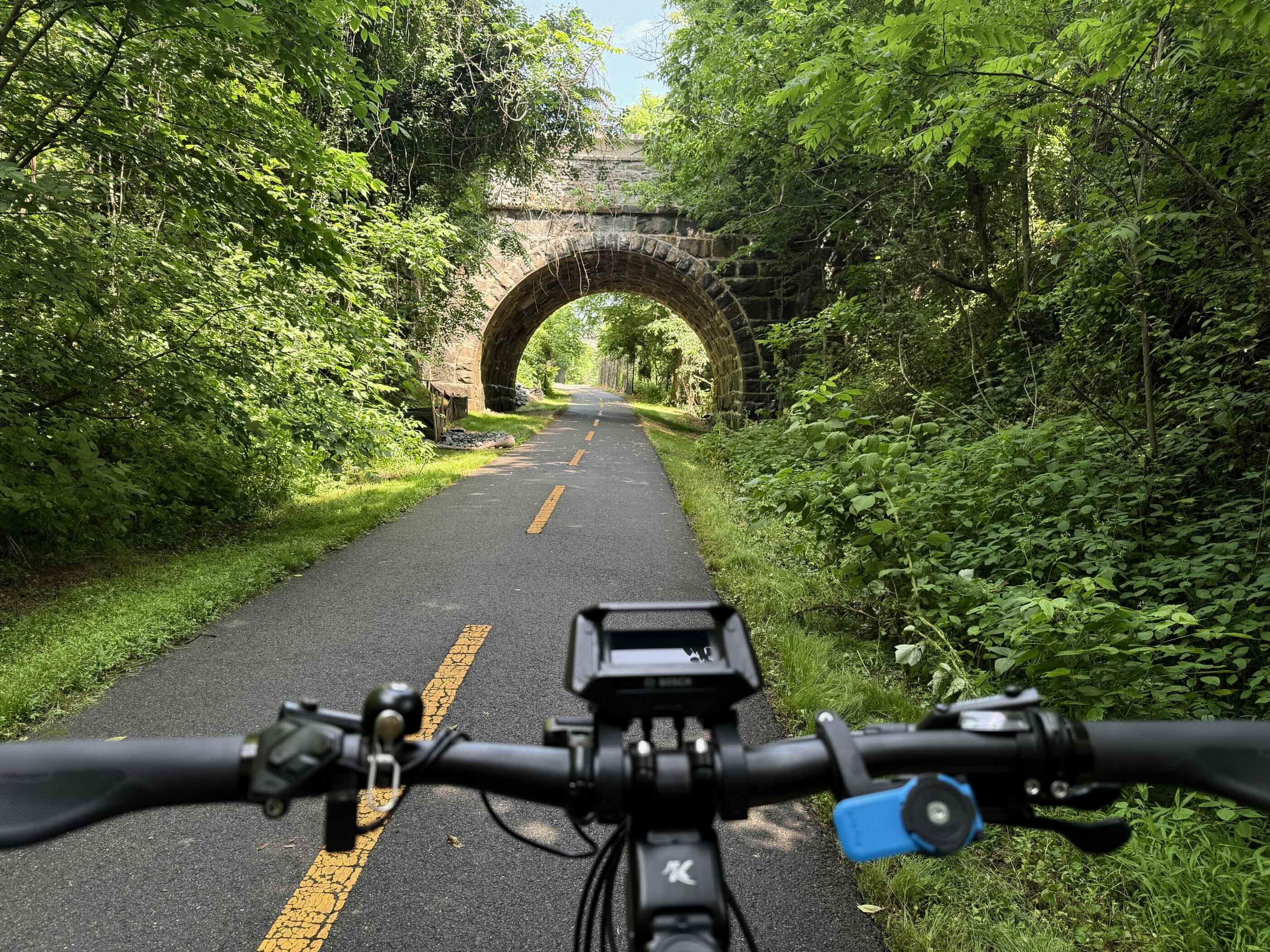 A bike path through trees leading toward a stone bridge
