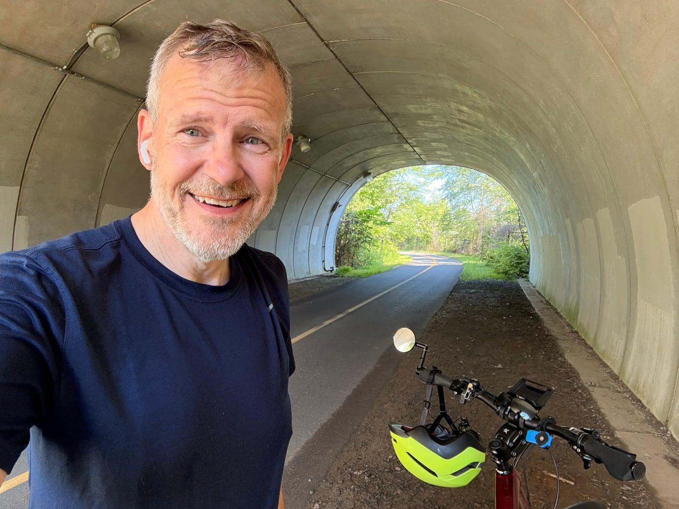 Joe with his bicycle in a tunnel opening onto a tree-lined trail.